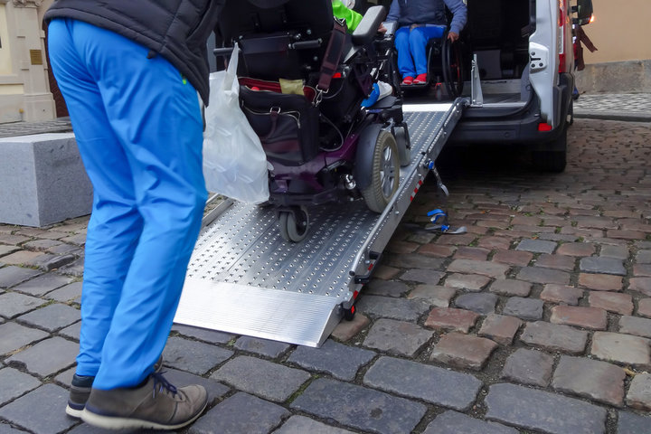 carer pushing wheelchair user into a car adapted for wheelchair users